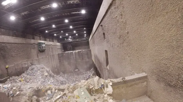 Avfallsbunker inifrån med betongväggar, avfall och kranbana, drönarbild